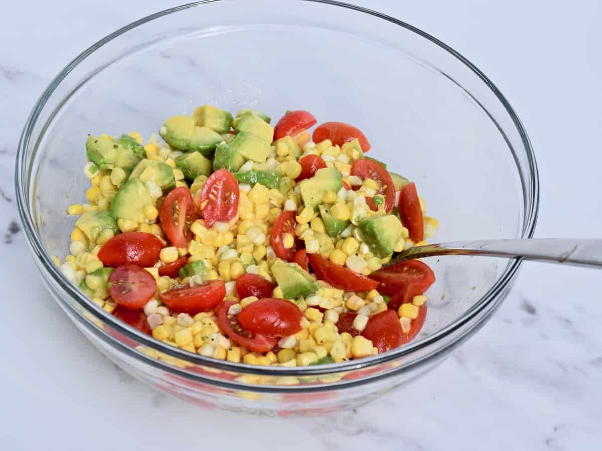 Corn kernels, halved grape tomatoes, chopped avocado in a glass bowl..