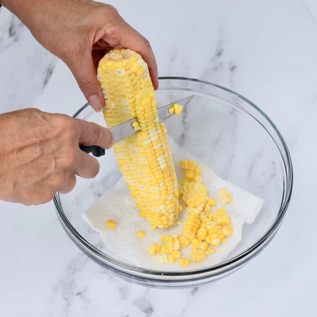 Hand cutting corn off the cob into a bowl.
