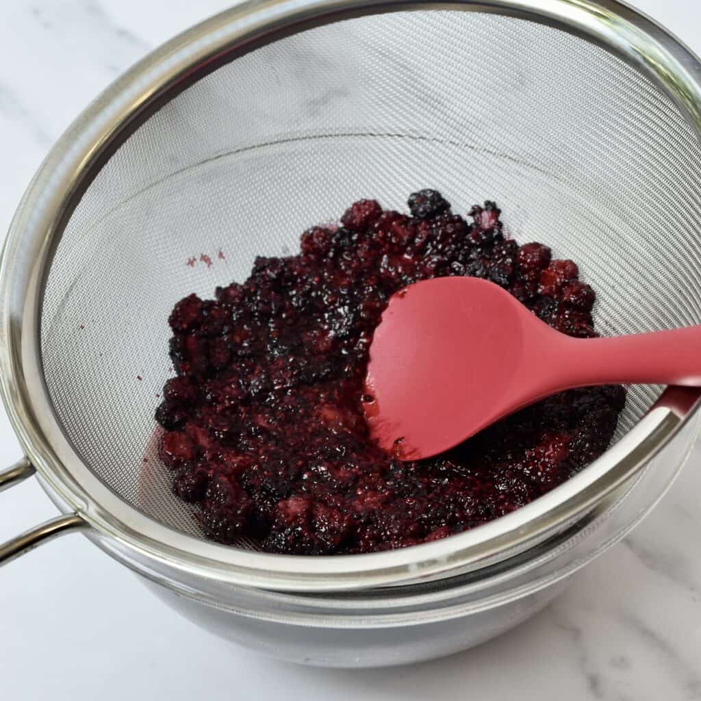 Mashing cooked blackberries in a fine mesh strainer.