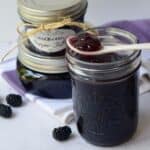 Blackberry Pepper Jelly with white spoonful balancing on top sitting on purple cloth.