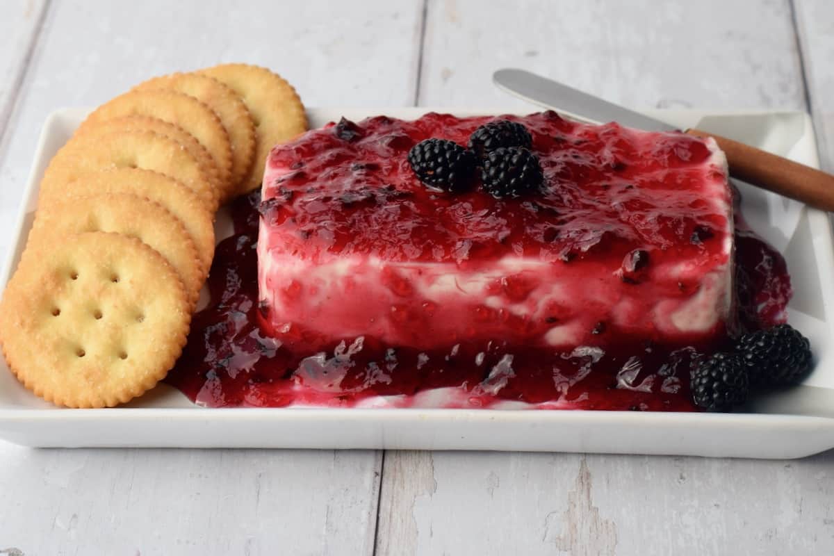 Blackberry Pepper Jelly with block of cream cheese with crackers on the left and fresh blackberries on top.