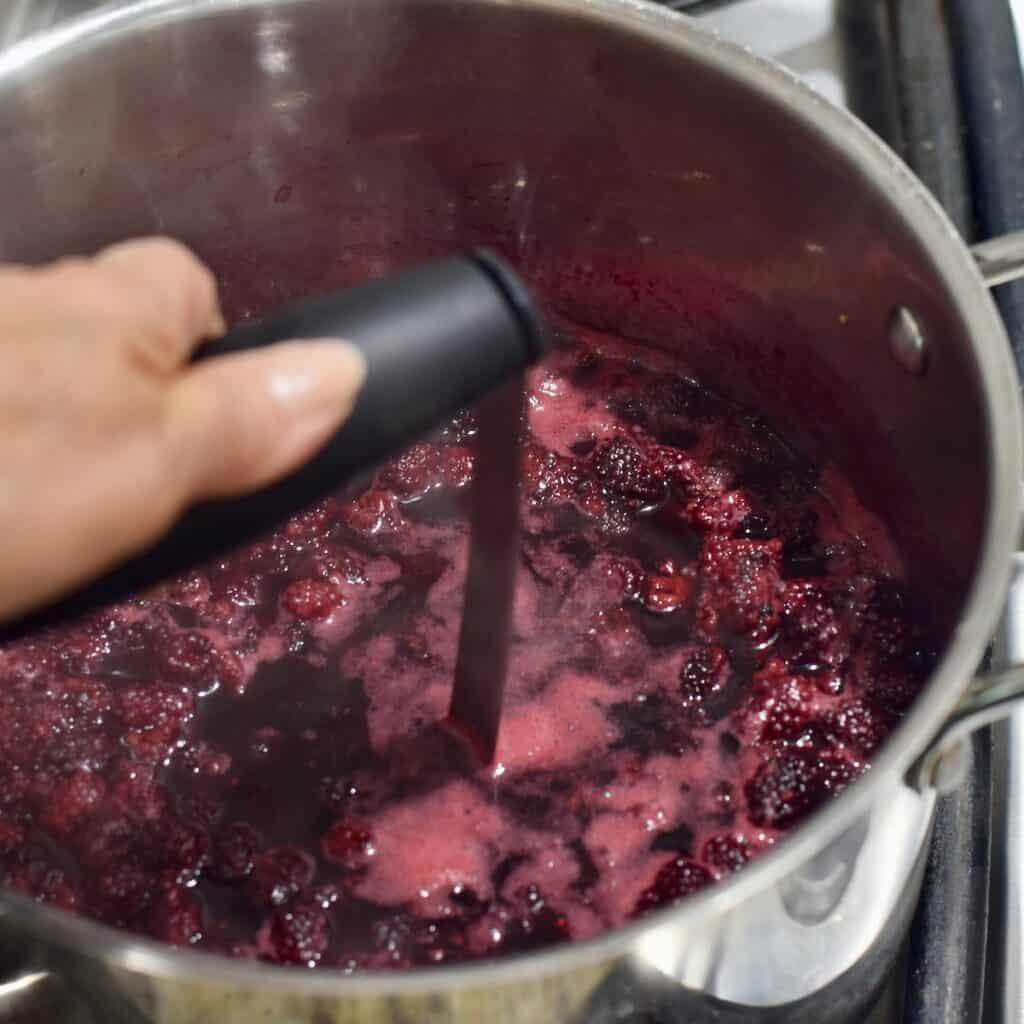 Mashing cooked blackberries in pot with potato masher