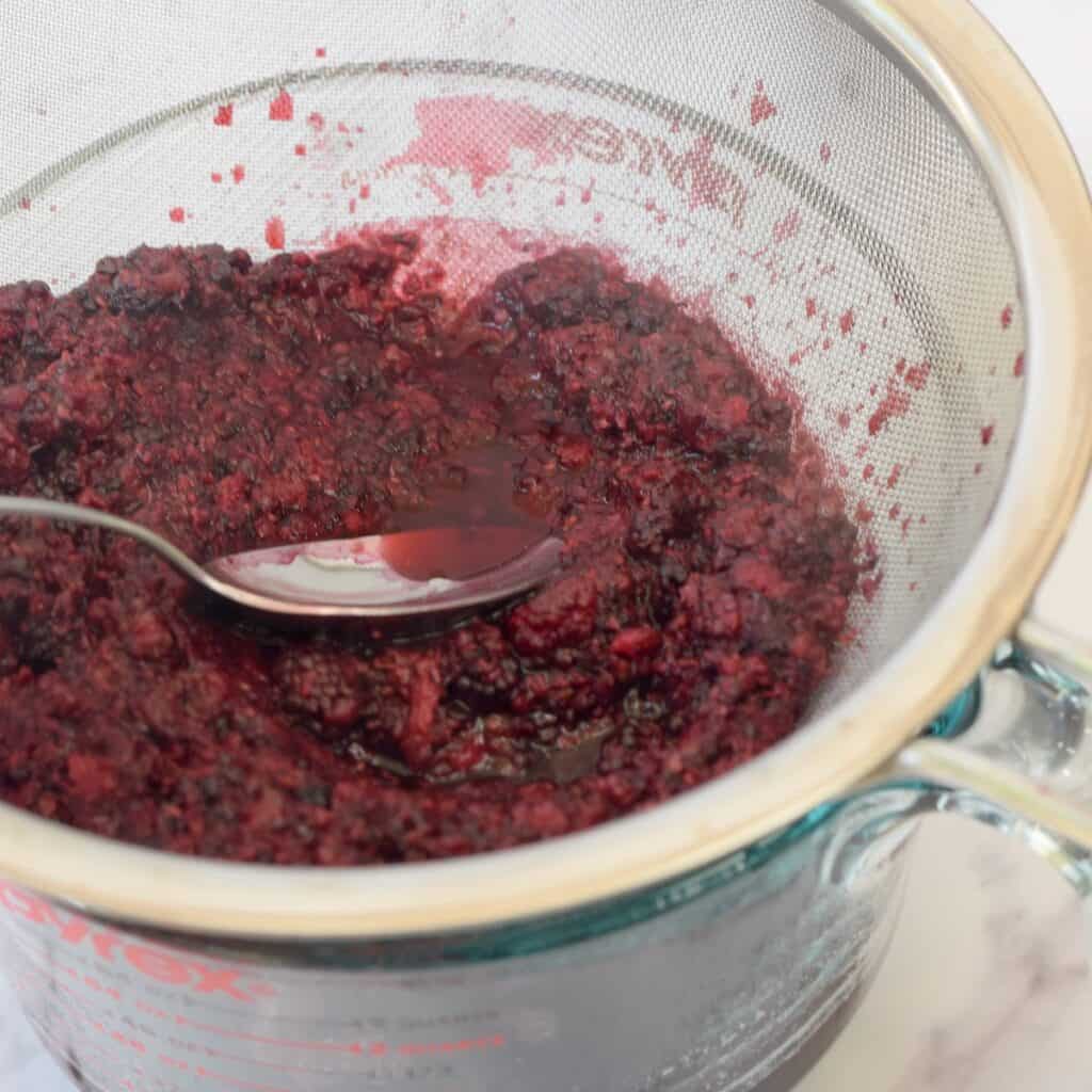 Pressing juice out of blackberry seeds in mesh strainer