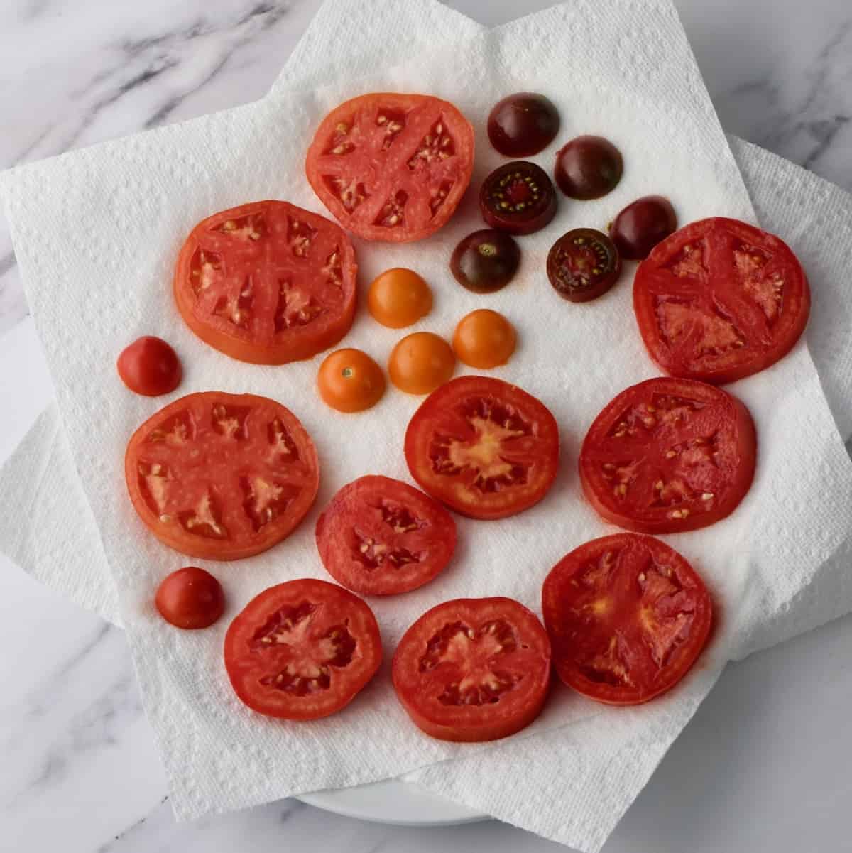 Sliced tomatoes of different sizes draining on paper towels.