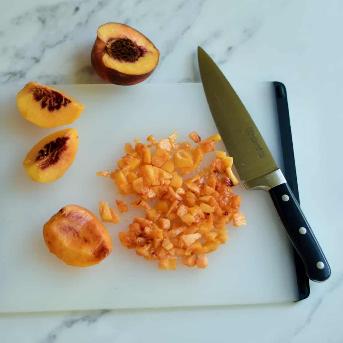Chopped fresh peaches on a cutting board with a knife.