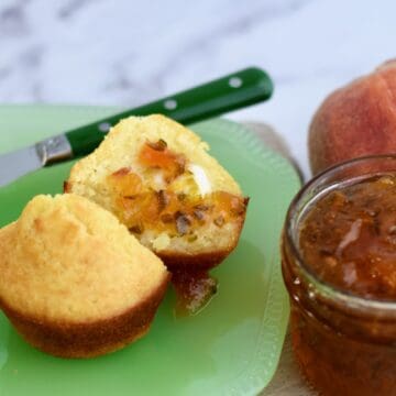 Cornbread muffin cut in half with butter and peach pepper jelly spread on it.