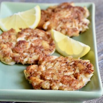 Three crab cakes on a green platter with lemon wedges.