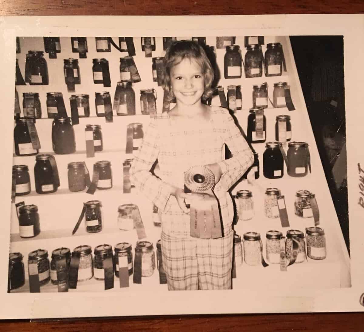 Child holding a jar with a grand champion ribbon on it. Canning jars in the background.