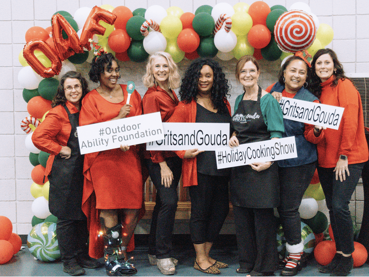 Seven ladies dressed in Christmas colors in front of red and green balloon arch.
