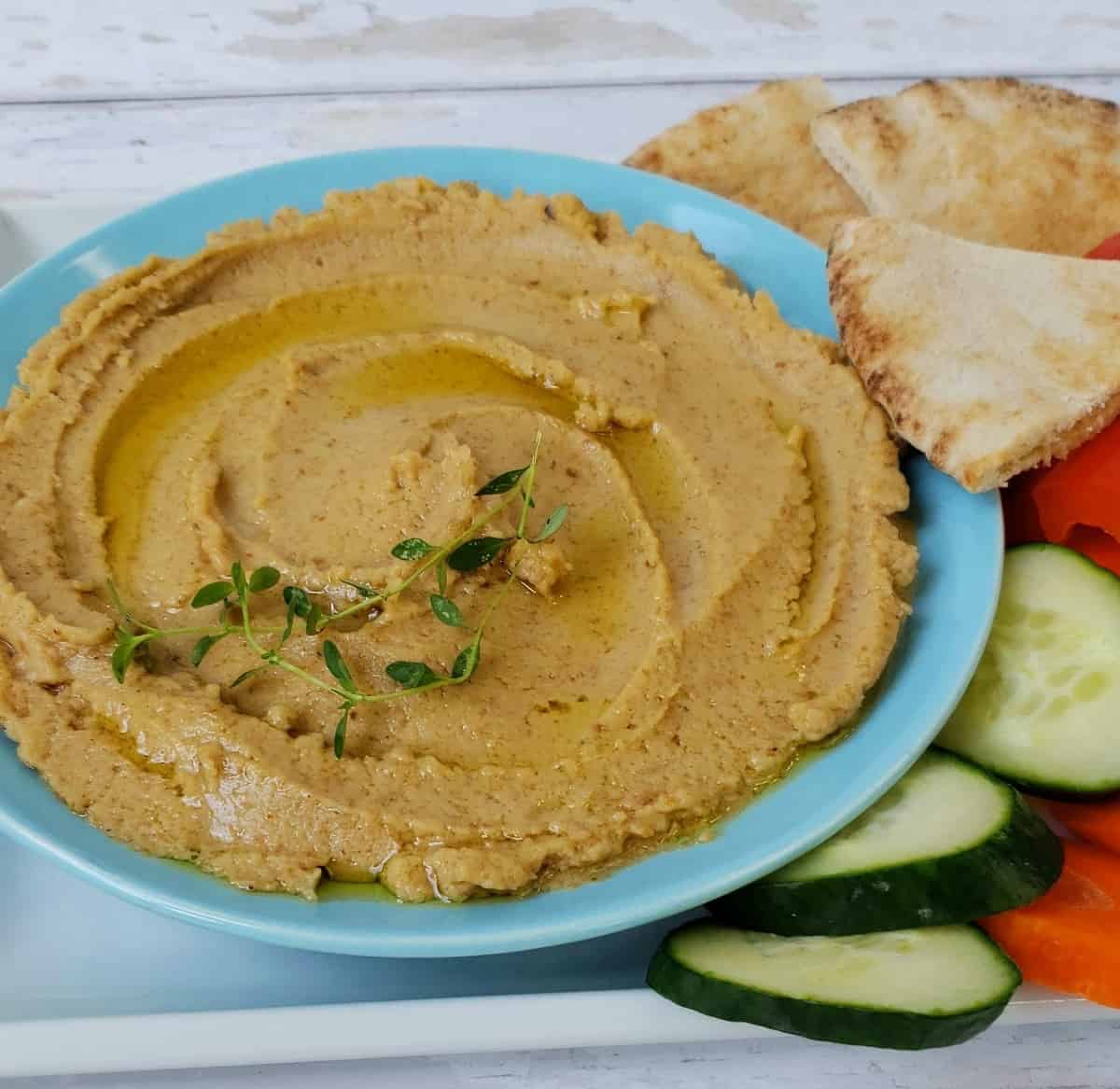 Peanut hummus spread on blue plate with pita chip on the right side.