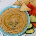 Overhead view of Boiled Peanut Hummus in blue bowl with pita chip and vegetables on the side.