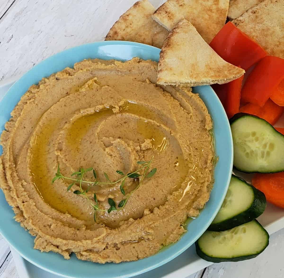 Overhead view of Boiled Peanut Hummus in blue bowl with pita chip and vegetables on the side.