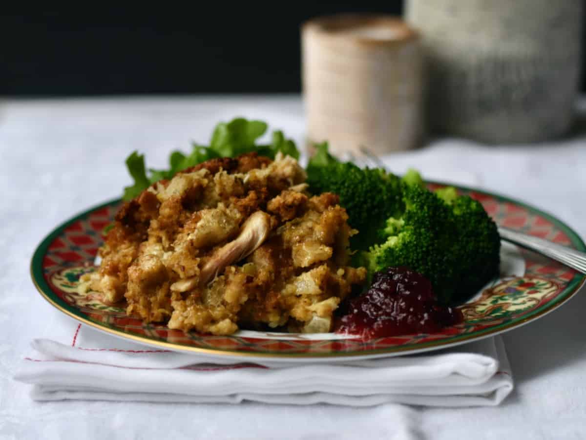 Serving of chicken cornbread dressing with candles in background cranberry sauce on plate.
