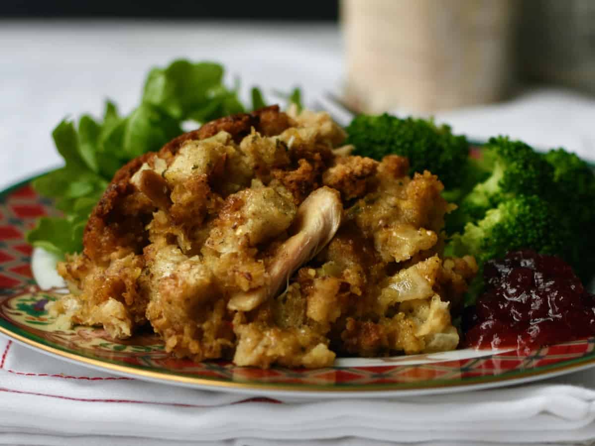 Serving of chicken cornbread dressing on plate with broccoli and salad.