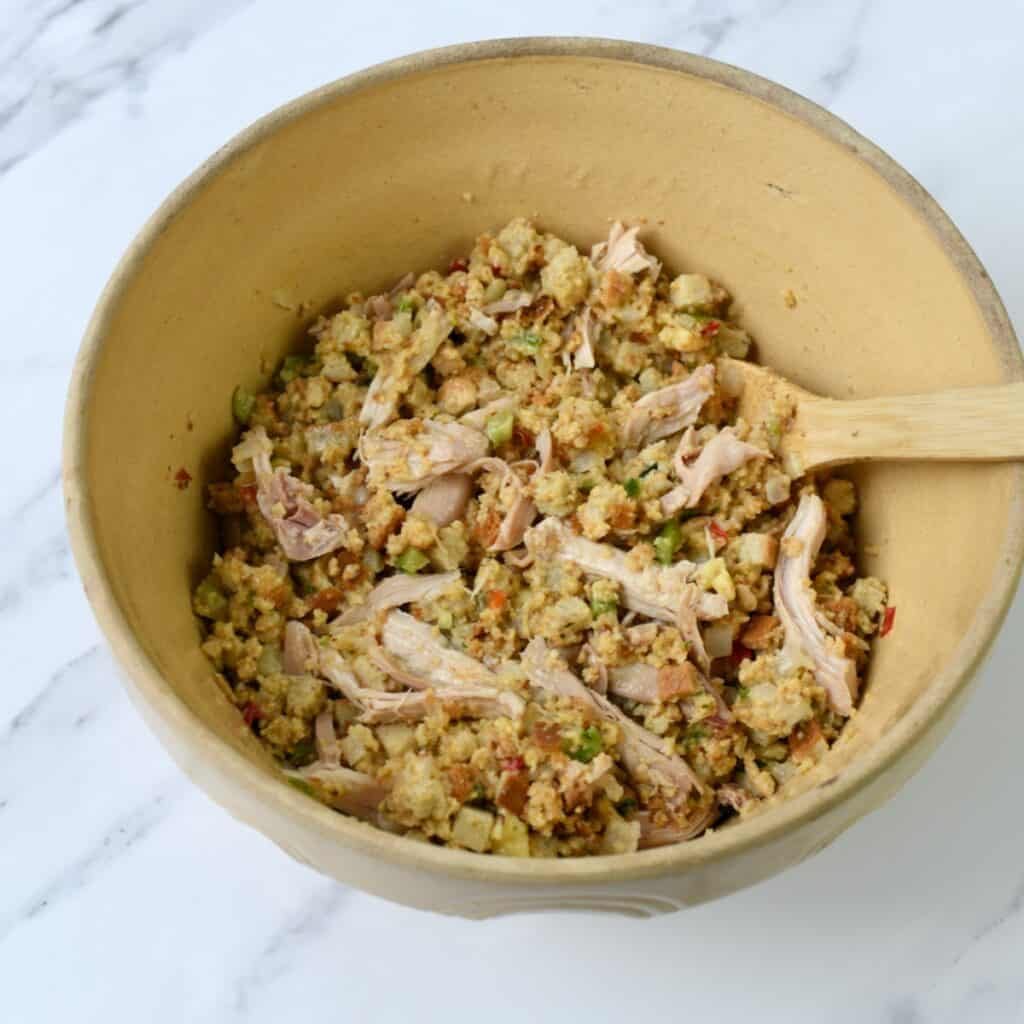 Chicken and cornbread dressing uncooked in tan bowl with wooden spoon.
