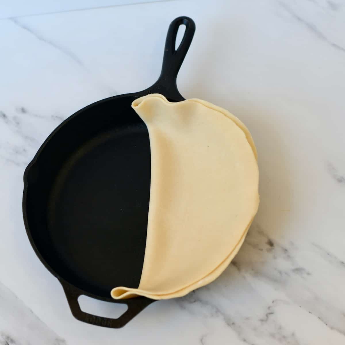 Unbaked pie crust dough folded in half in a cast iron skillet.