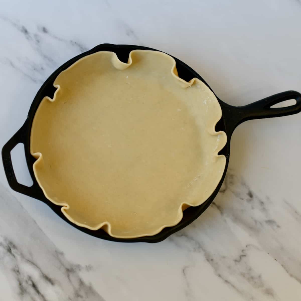 Unbaked pie crust fitted in to cast iron skillet.