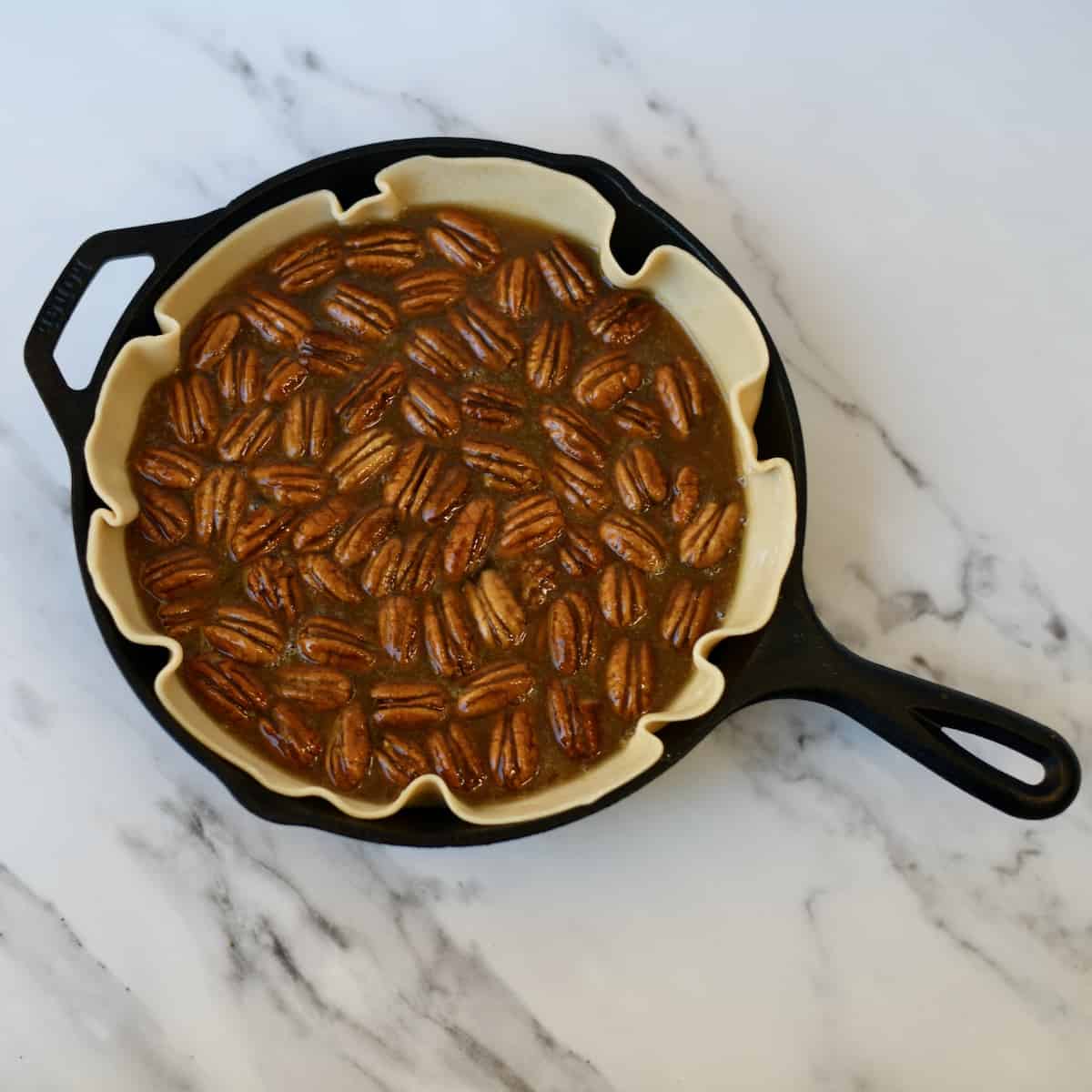 Pecans and filling in unbaked pie shell fitted in a cast iron skillet.