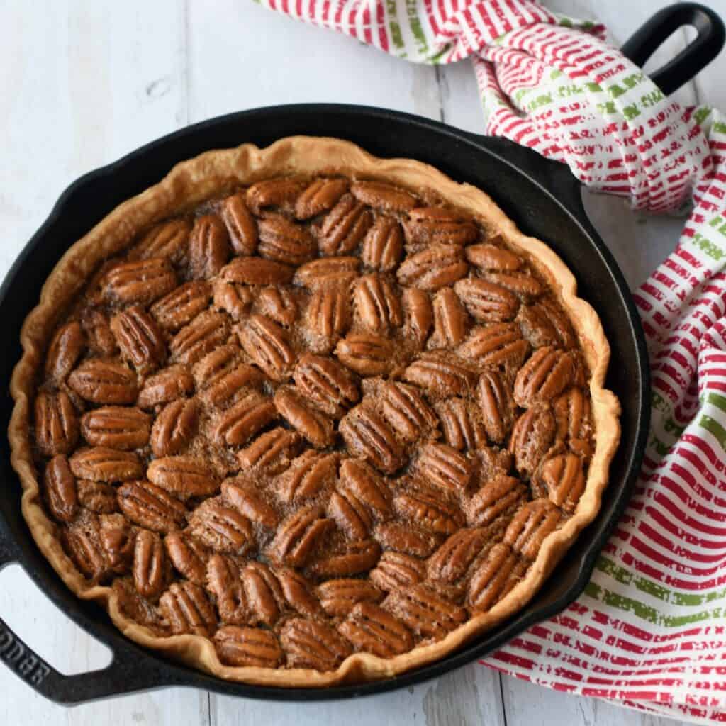 Overhead view of pecan pie in cast iron skillet with red and green cloth around handle.