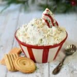 Little Debbie Christmas tree cake sticking out of red striped bowl of dip with cookies on white wood surface.