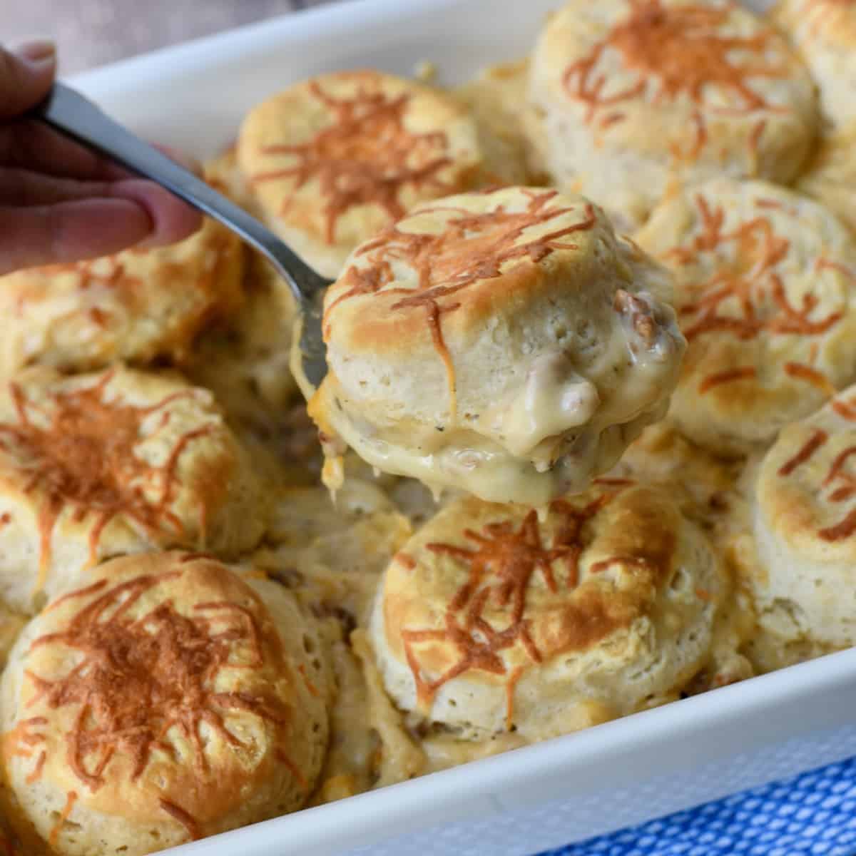 A biscuit being lifted from middle of casserole dish with sausage gravy underneath.