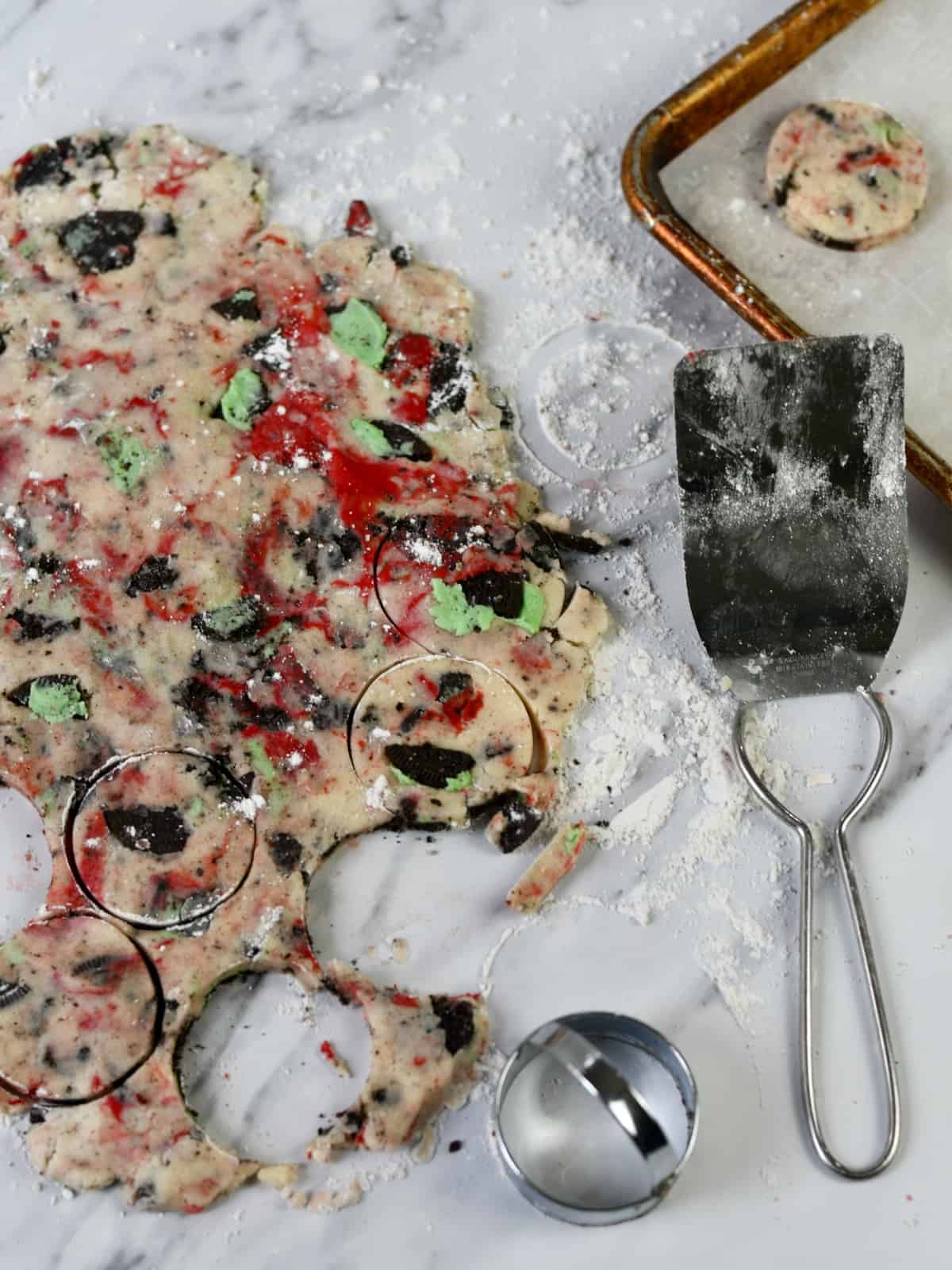Red and green cookies in cookie dough rolled out with spatula on side.