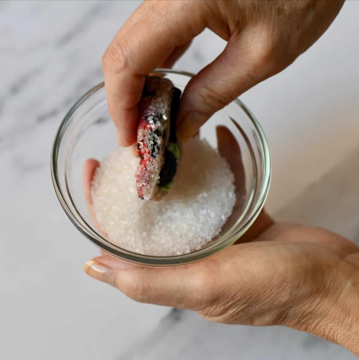 Hands rolling edges of cookies in sugar.