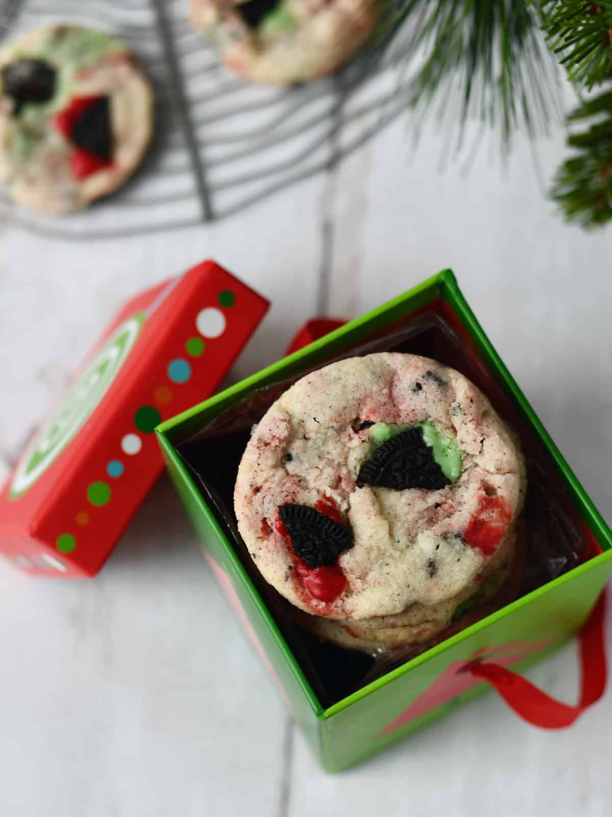 Overhead view of a stack of red and green cookies and cream shortbread cookies in a Christmas gift box with lid to the side.