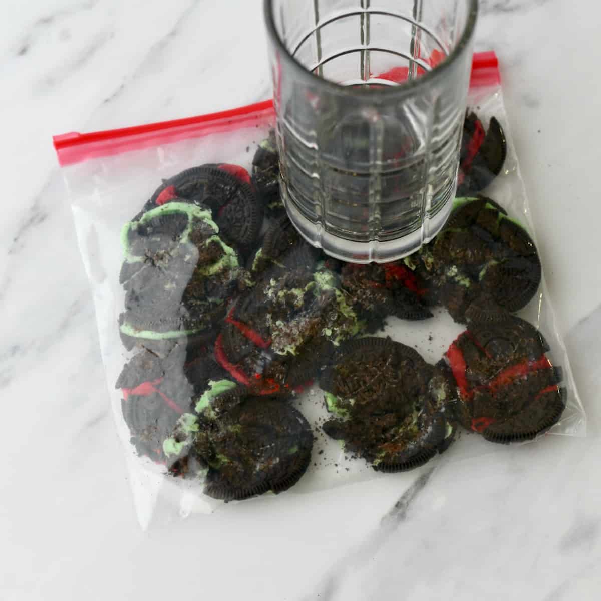 Highball glass on top of red and green Oreos cookies in a zip top plastic bag.