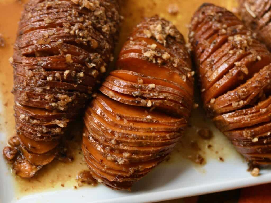 Three hasselback sweet potatoes on a white plate with pecans on top.