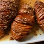Three hasselback sweet potatoes on a white plate with pecans on top.