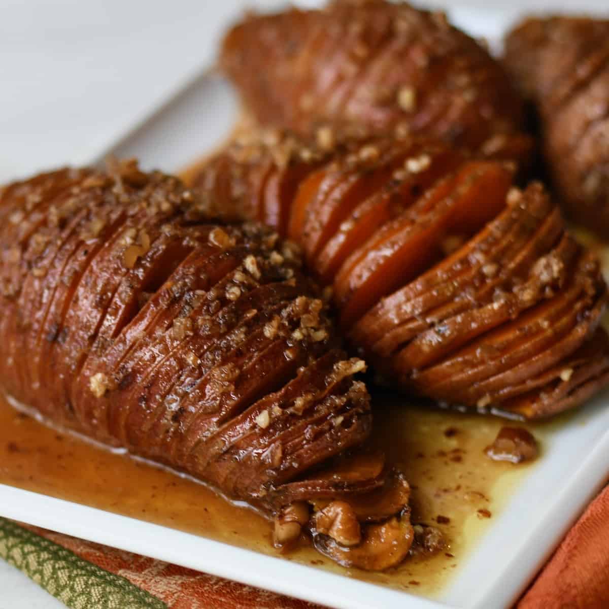 Close up hasselback sweet potatoes on a white platter with maple pecan butter drippings.