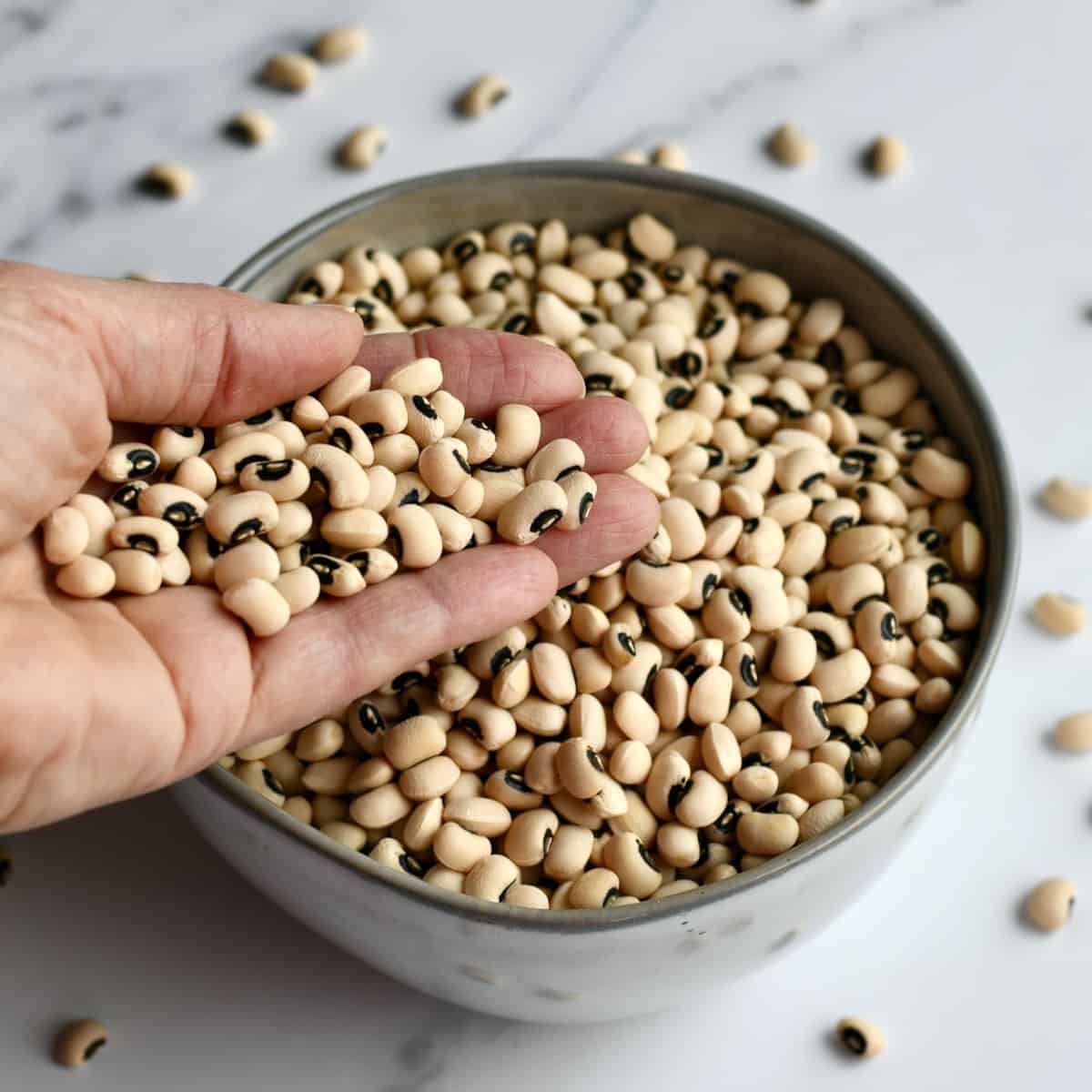 Hand pouring dried black eyed peas in bowl of peas.