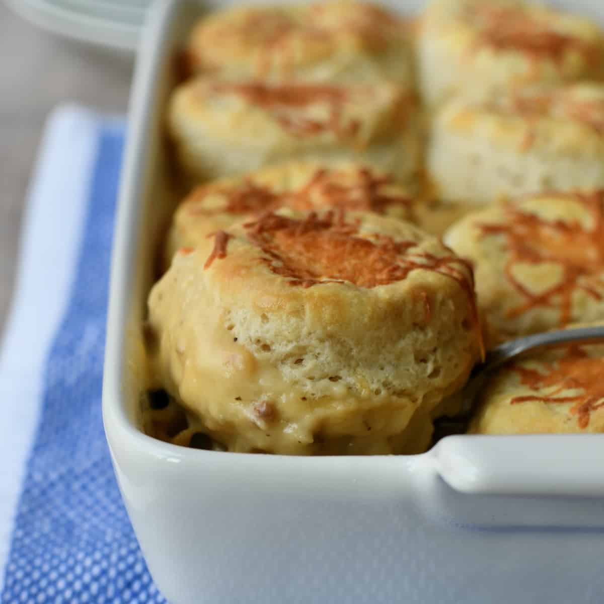 Cheesy biscuit lifted out of white casserole dish.
