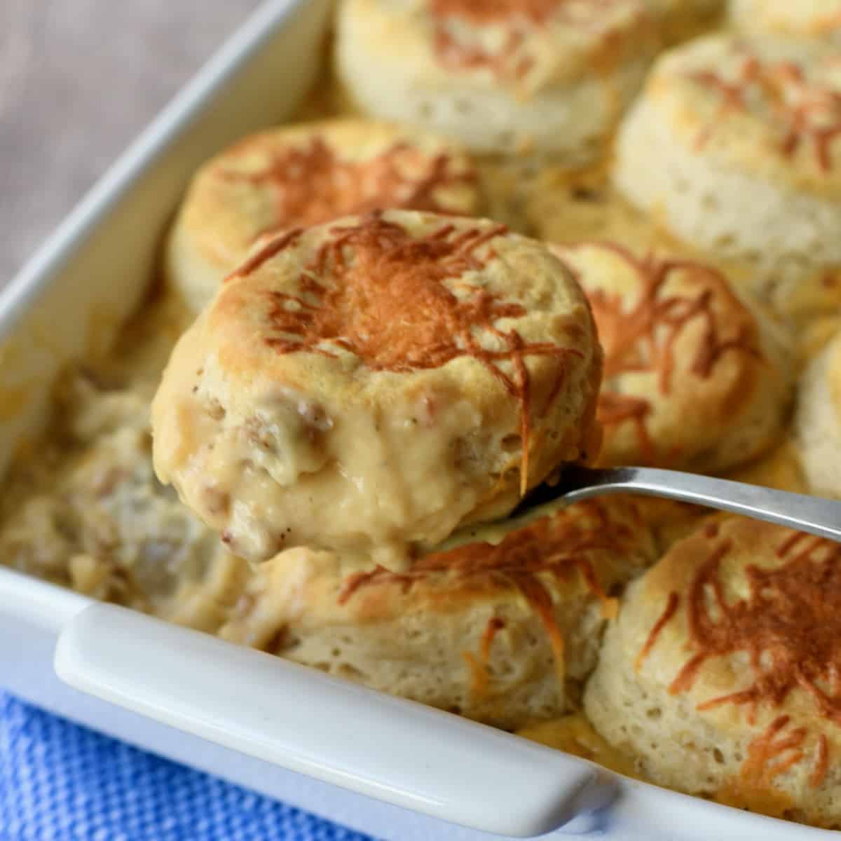 Biscuit being lifted out of casserole dish with sausage gravy on bottom.