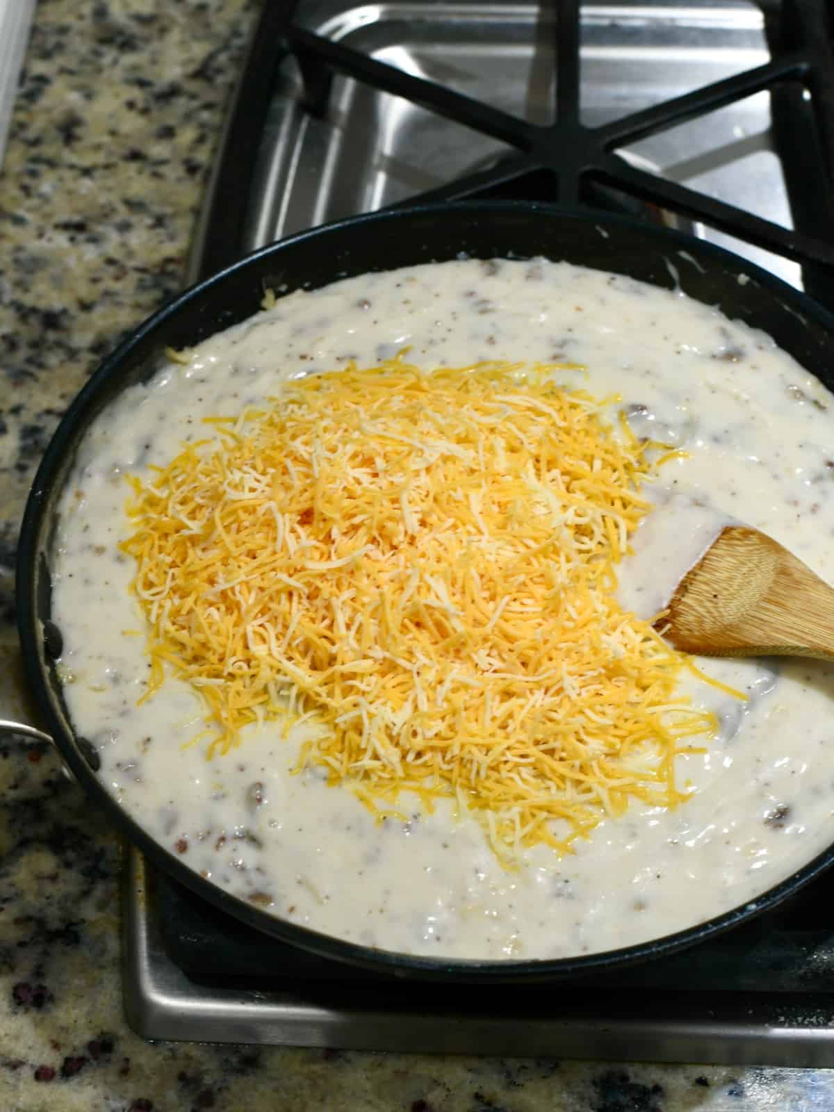Cheese on top of sausage gravy in a skillet.