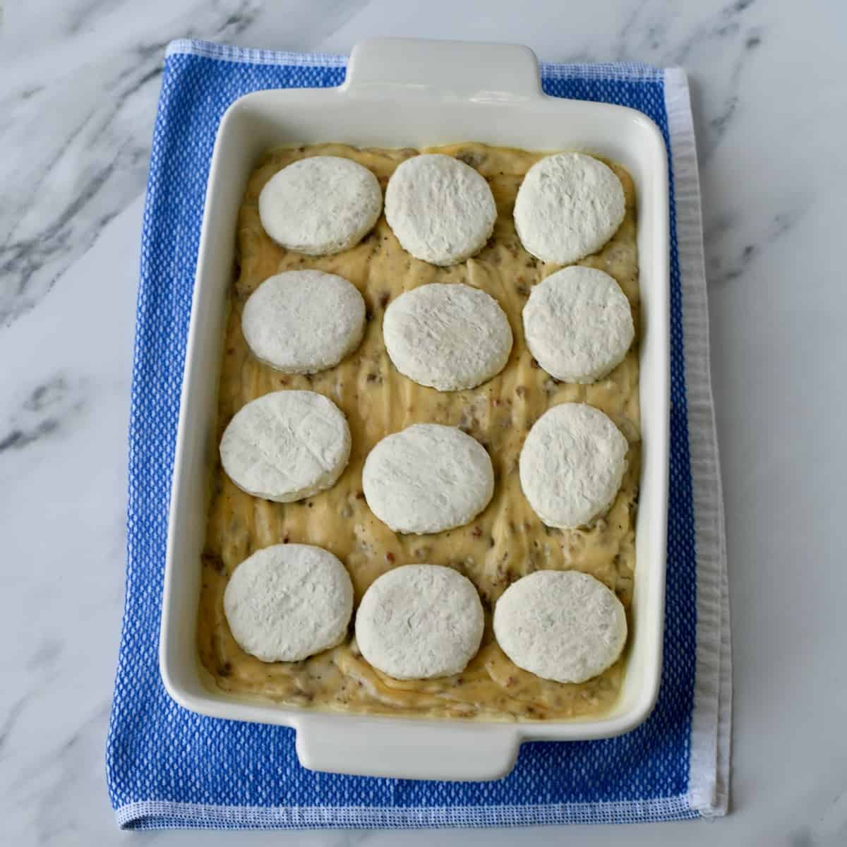 Frozen biscuits on sausage gravy in a white casserole dish.