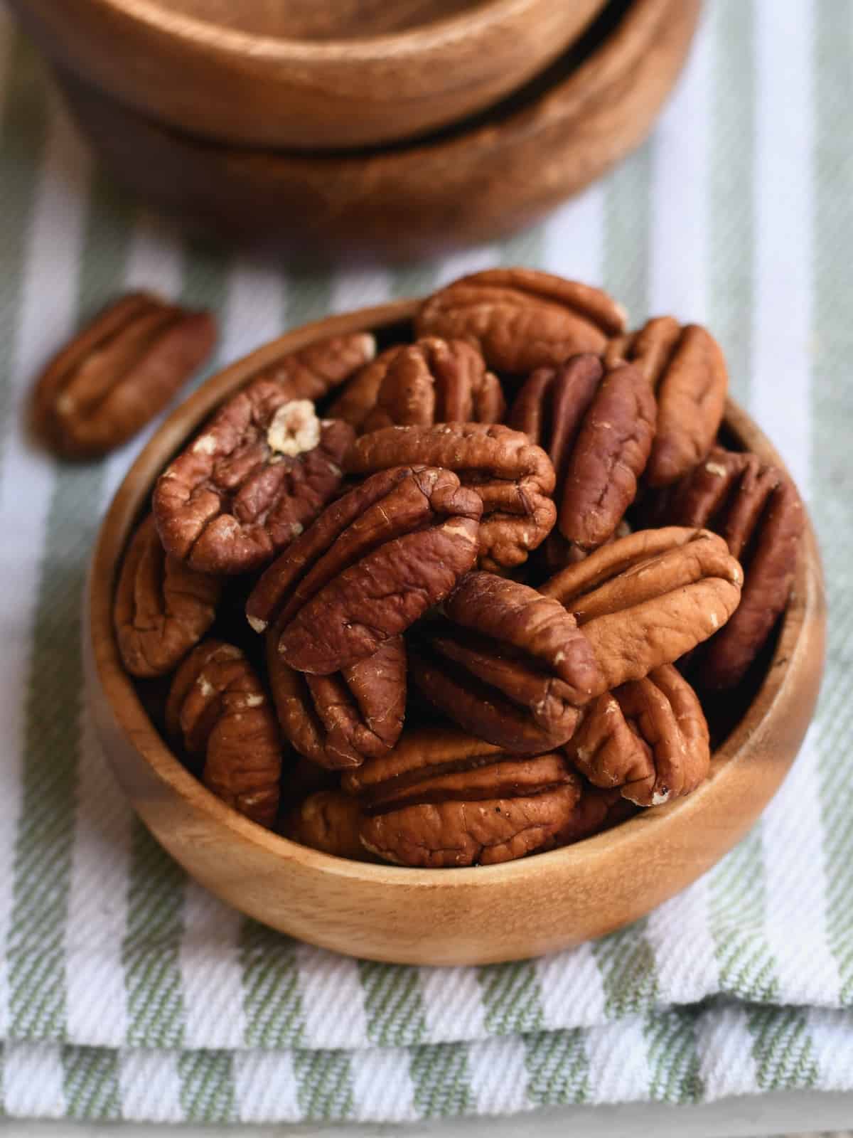Wooden bowl of pecan halves with stack of wooden bowls above it.