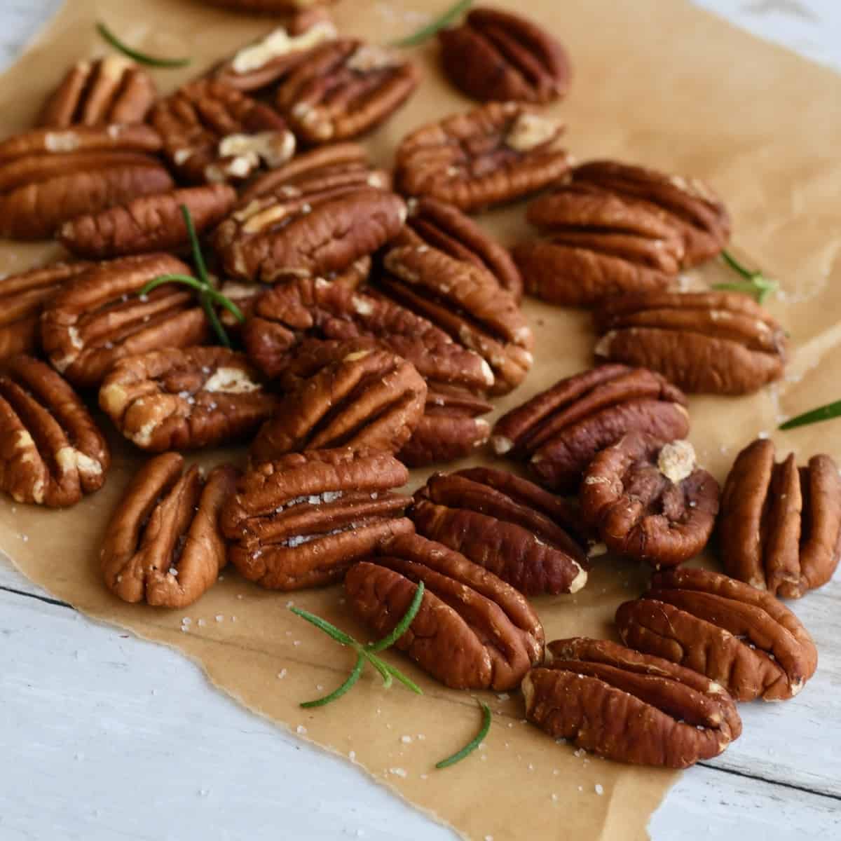 Pecan halves with salt and rosemary on brown parchment paper.