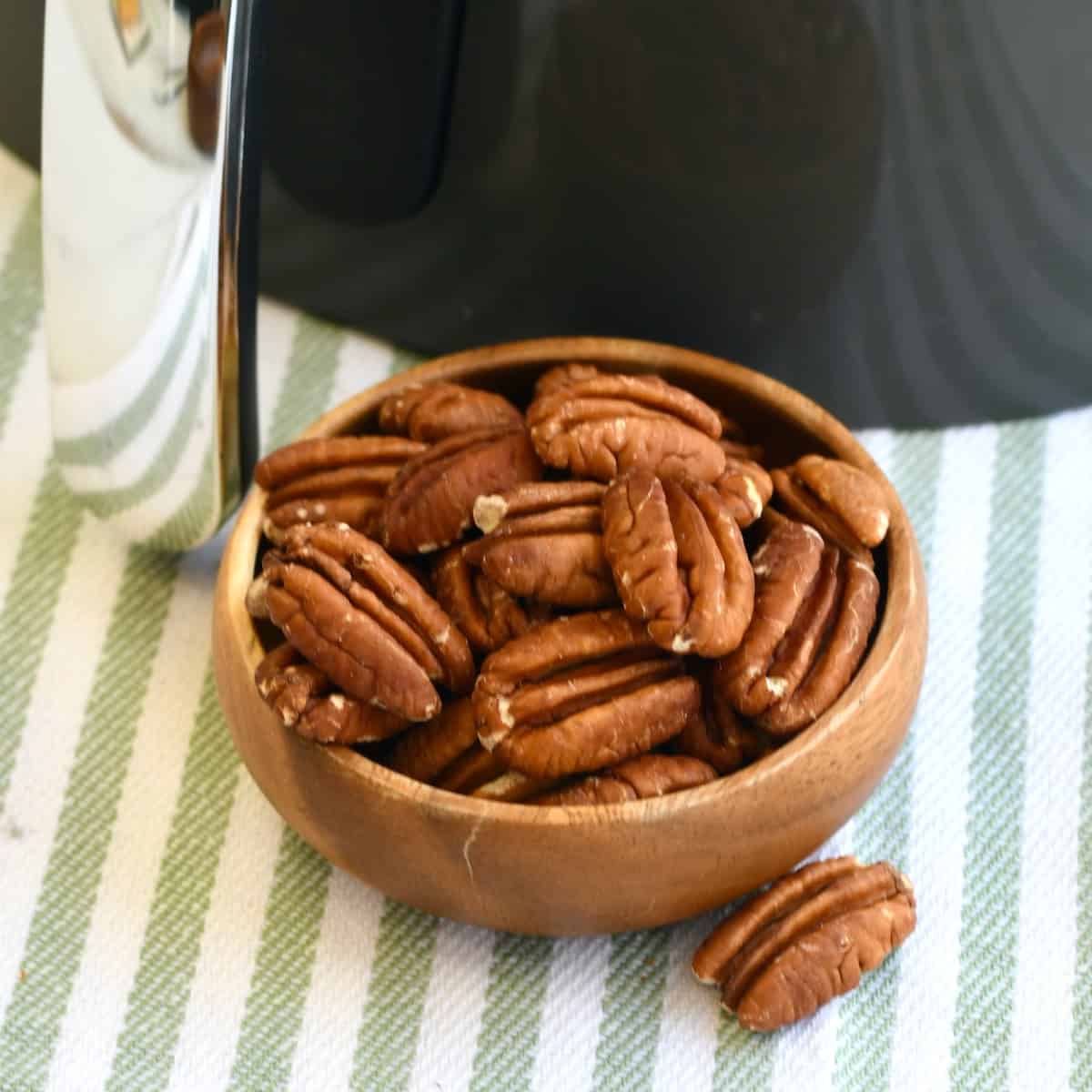 Wooden bowl of pecan halves in front of an air fryer.