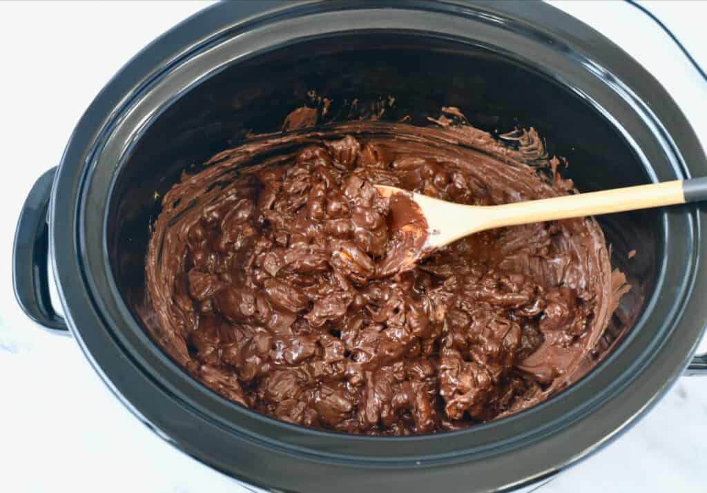 Melted chocolate and pecans in a Crockpot stirred with a wooden spoon.
