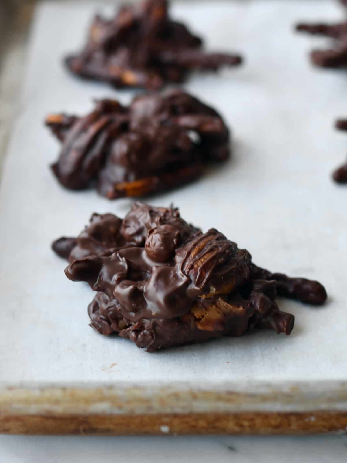 Dark chocolate pecan and pretzel clusters dropped on parchment paper on baking sheet close up.
