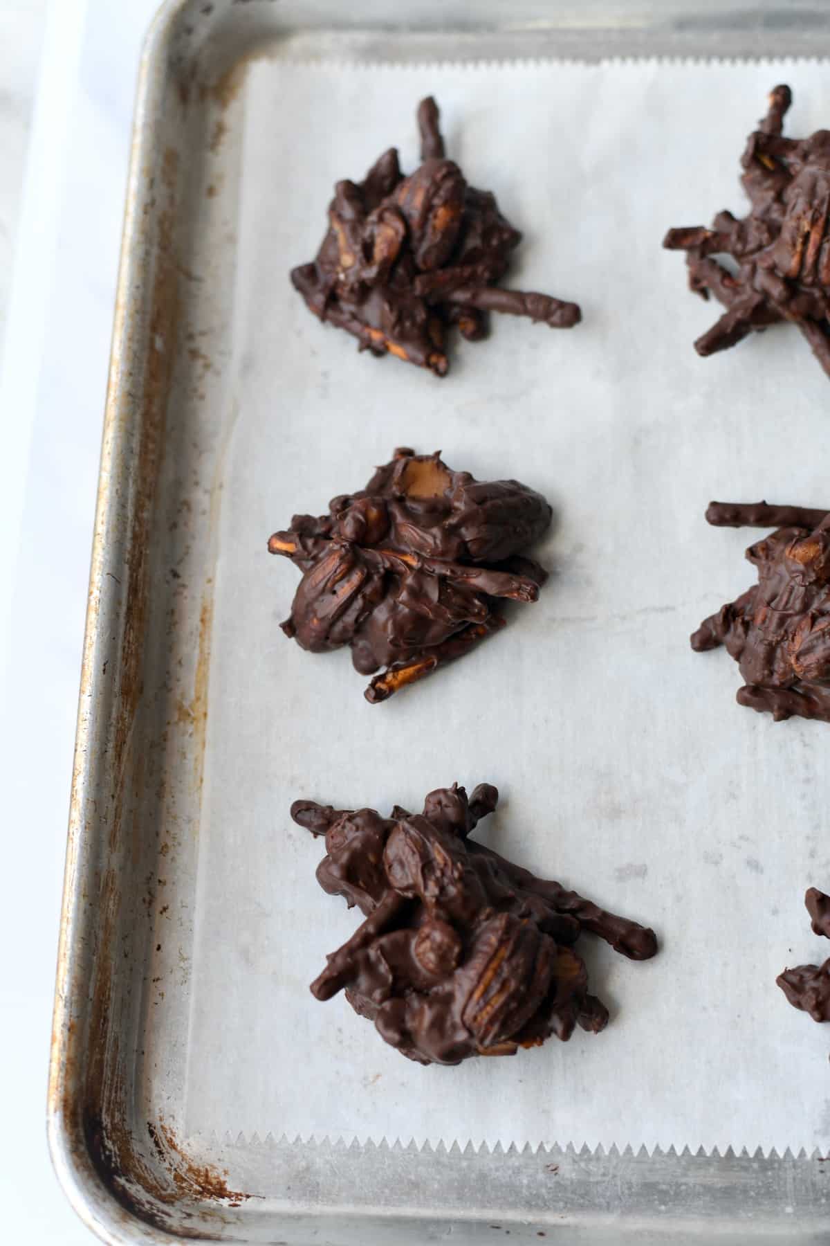 Dark chocolate pecan and pretzel clusters dropped on parchment paper on baking sheet.
