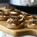 Crostini topped with cream cheese and instant pot bacon jam on a wooden serving board with Instant Pot in background