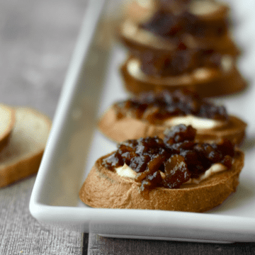 Close up image of crostini topped with cream cheese and instant pot bacon jam on a white platter