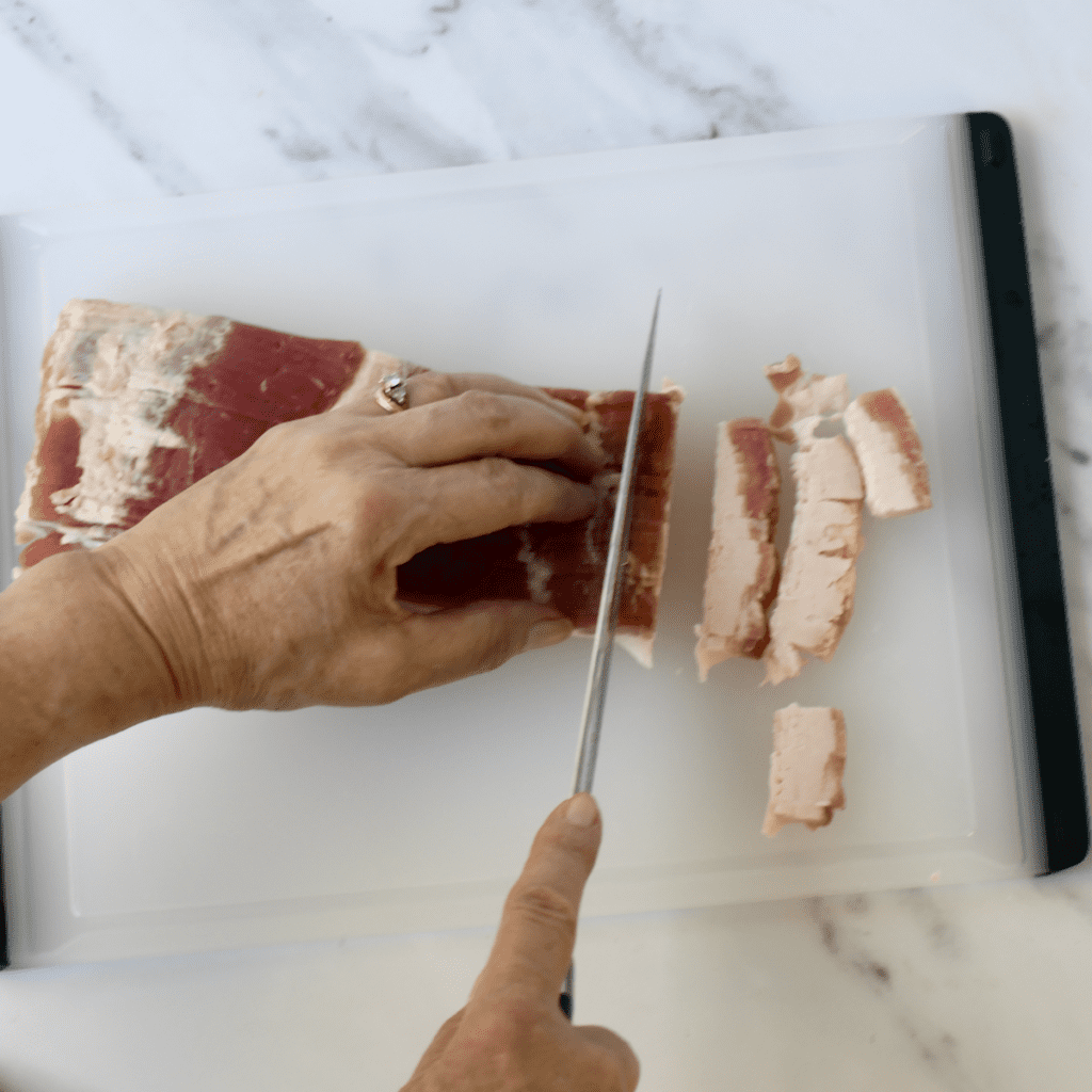Thick-cut bacon joint being chopped into small pieces on a chopping board