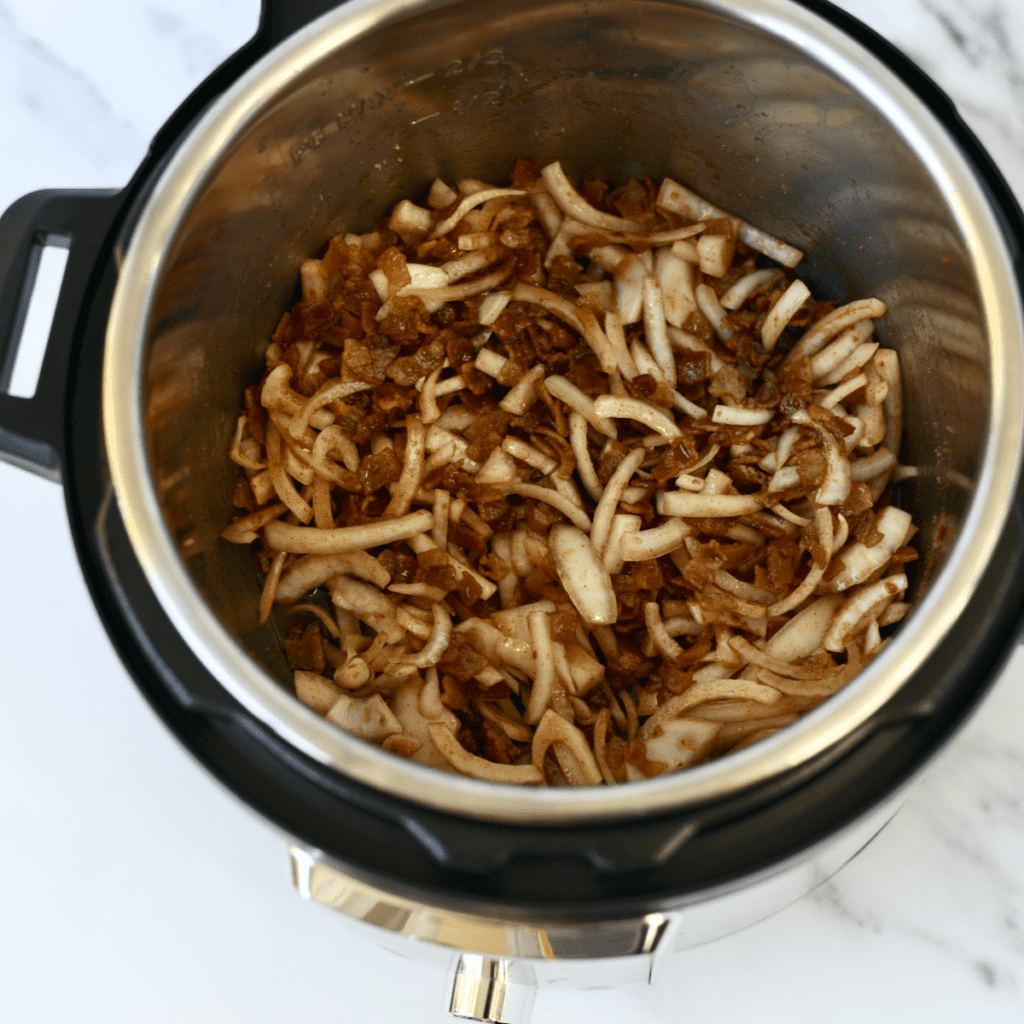 Instant Pot bowl filled with sliced onion, chopped bacon and spices