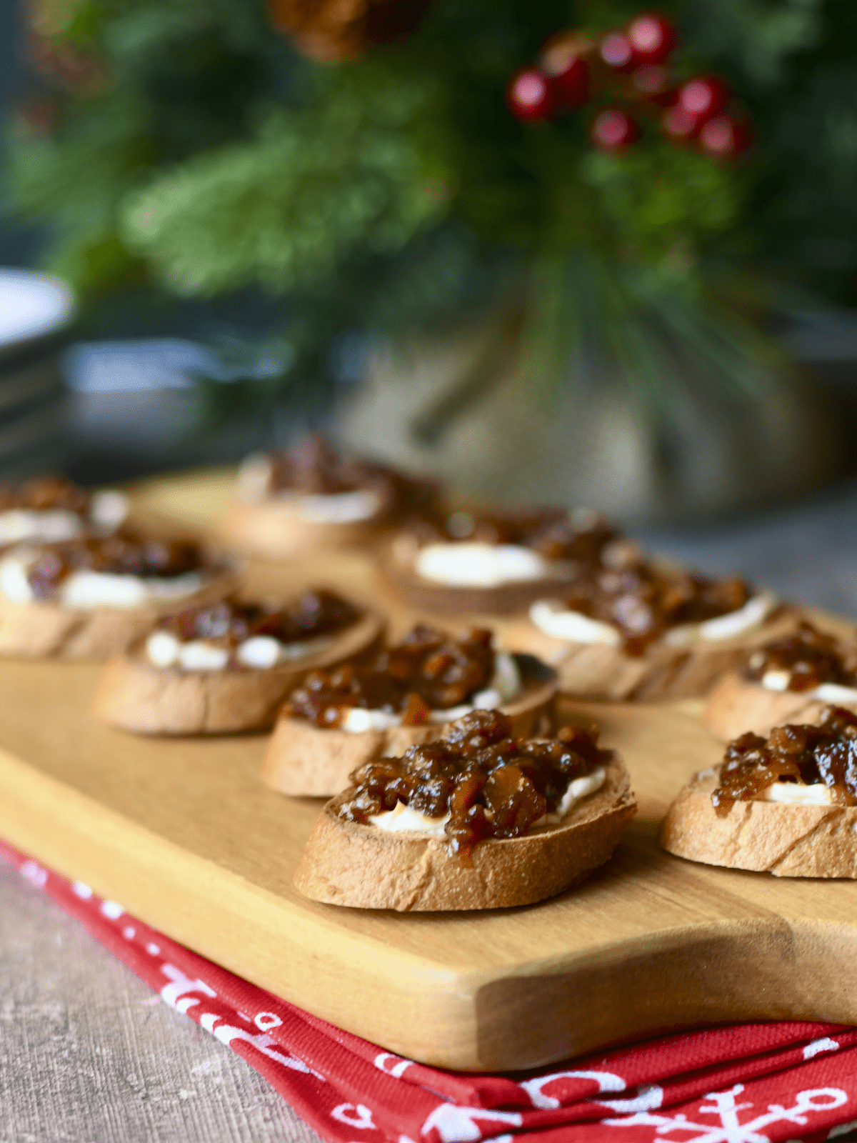 Crostini topped with cream cheese and instant pot bacon jam set on a wooden serving board under Christmas tree