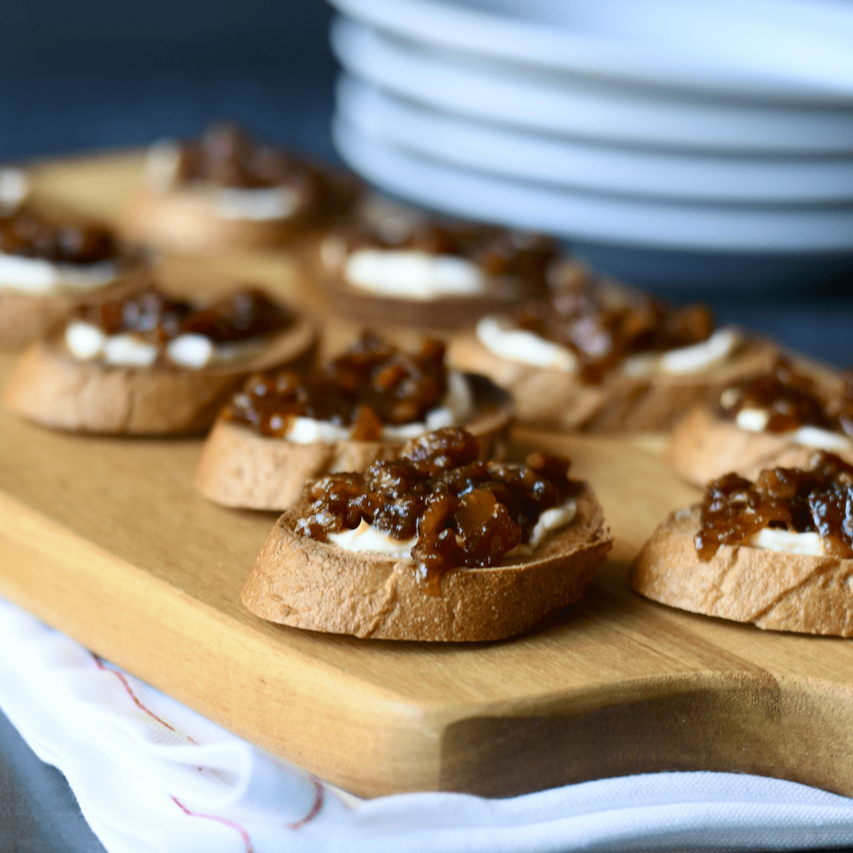 Crostini topped with cream cheese and instant pot bacon jam set on a wooden serving board