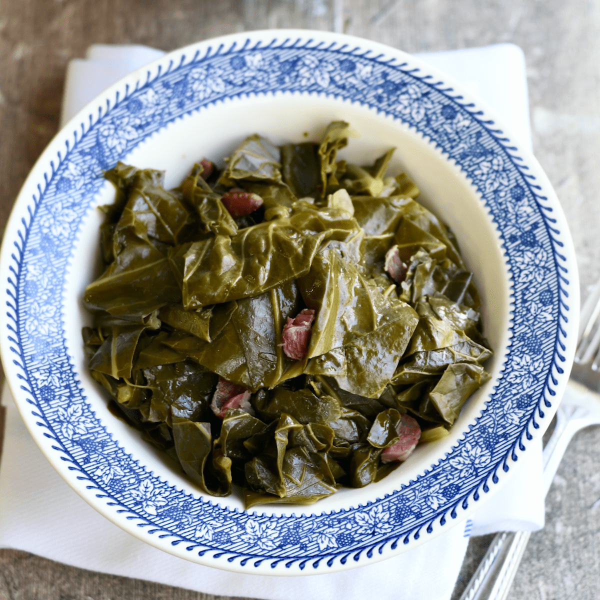 Blue rimmed bowl filled with collard greens and shredded ham hock